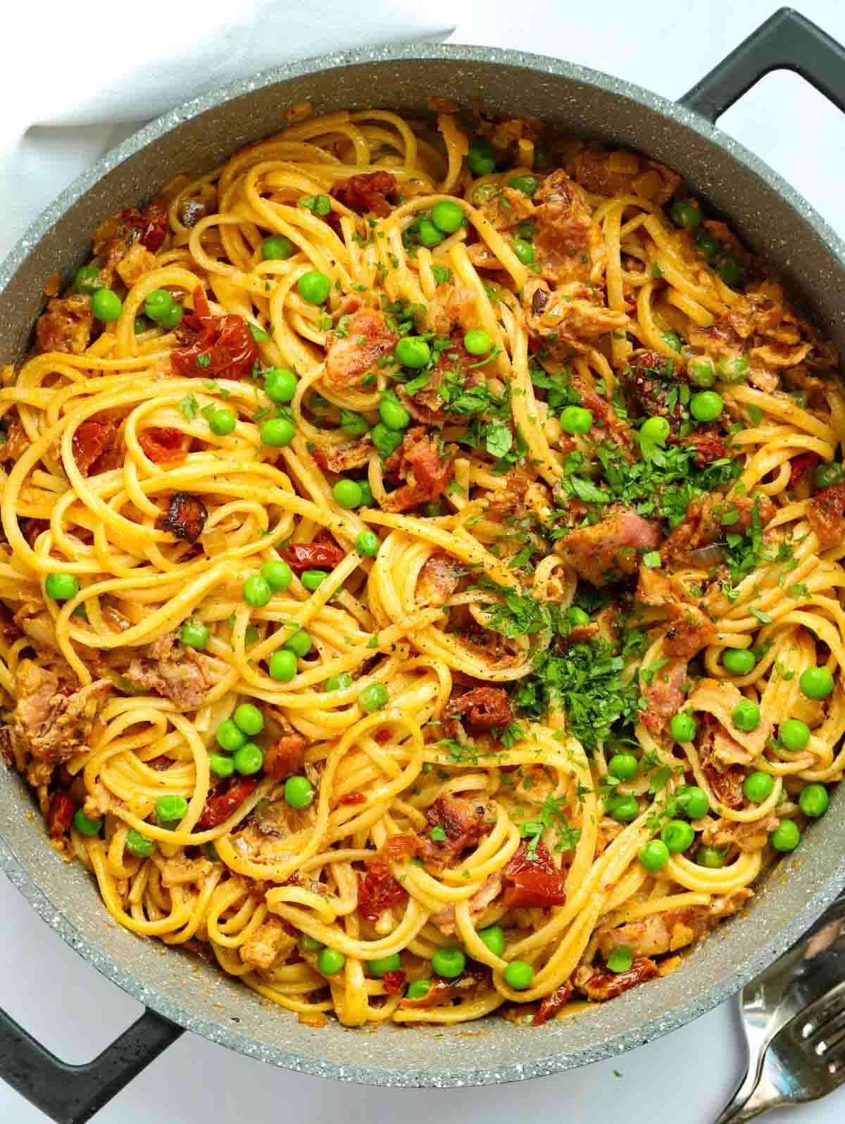 Una grande padella piena di spaghetti, pancetta e piselli per la ricetta della Pasta Cremosa con Pancetta.