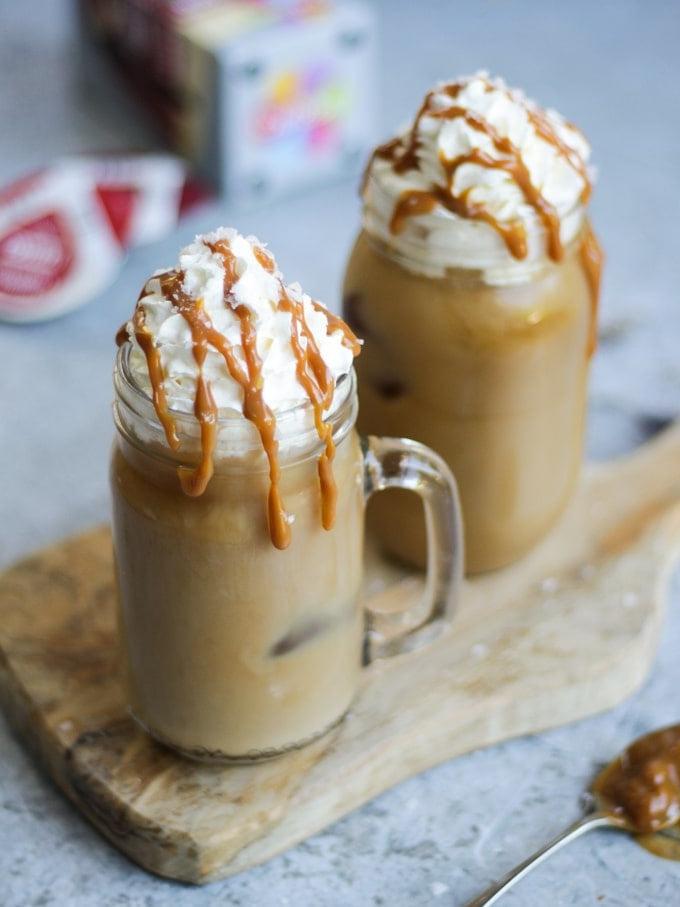 Due tazze di vetro con manico di caffè freddo con caramello salato e capsule Tassimo sullo sfondo grigio.