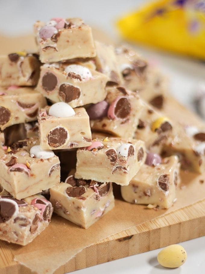 Pile di Mini Eggs Fudge per Pasqua tagliati a cubetti con mini uova in evidenza e confezione sullo sfondo.