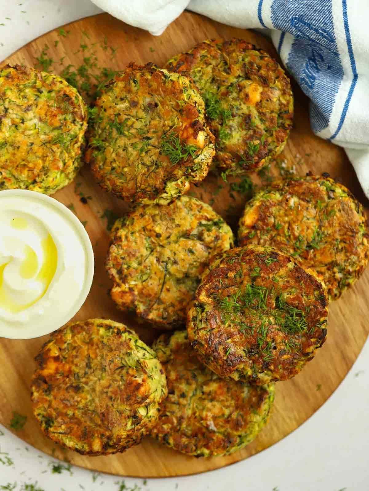 Otto frittelle di zucchine rotonde su un tagliere pronte per essere mangiate.