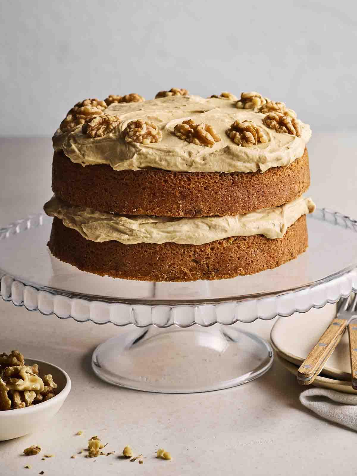 Un'alzata di vetro con una Torta al Caffè e Noci appena sfornata e splendidamente decorata.