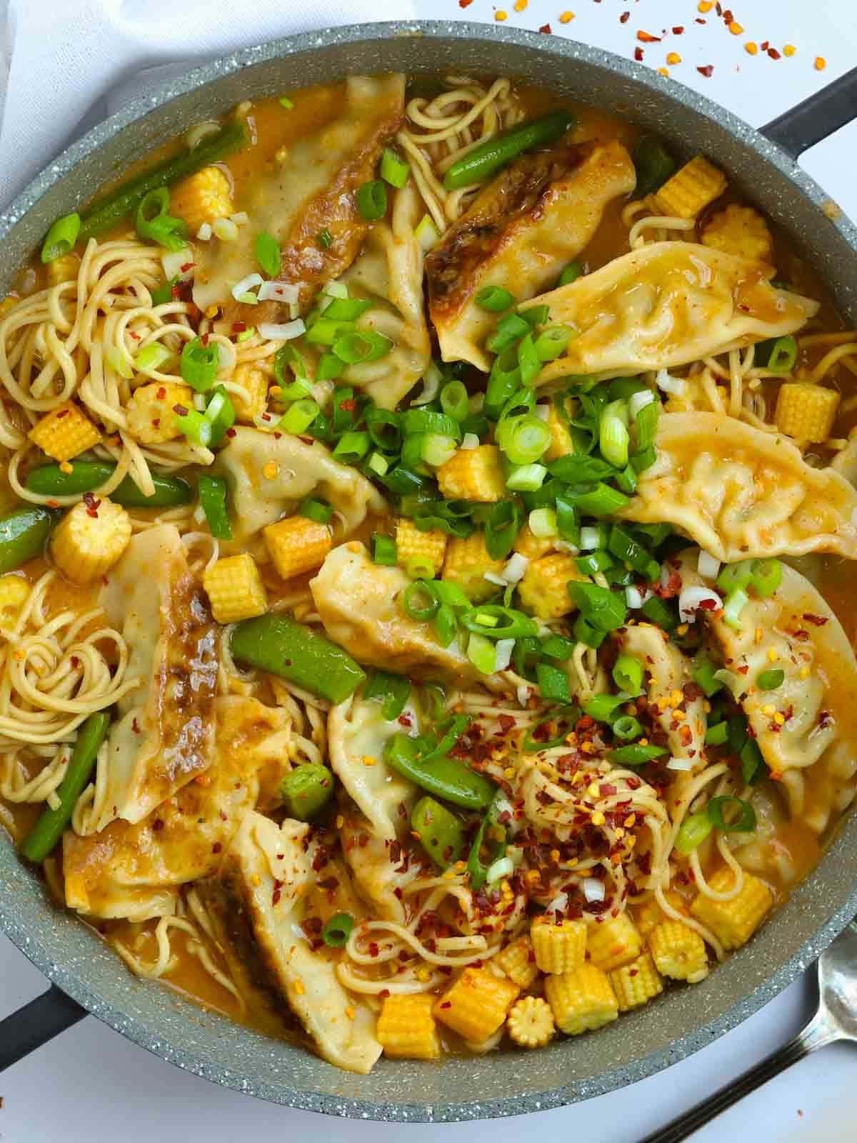 Una pentola piena di Zuppa di Gyoza cotta, con ravioli, noodles, fagioli, mais e cipollotti.