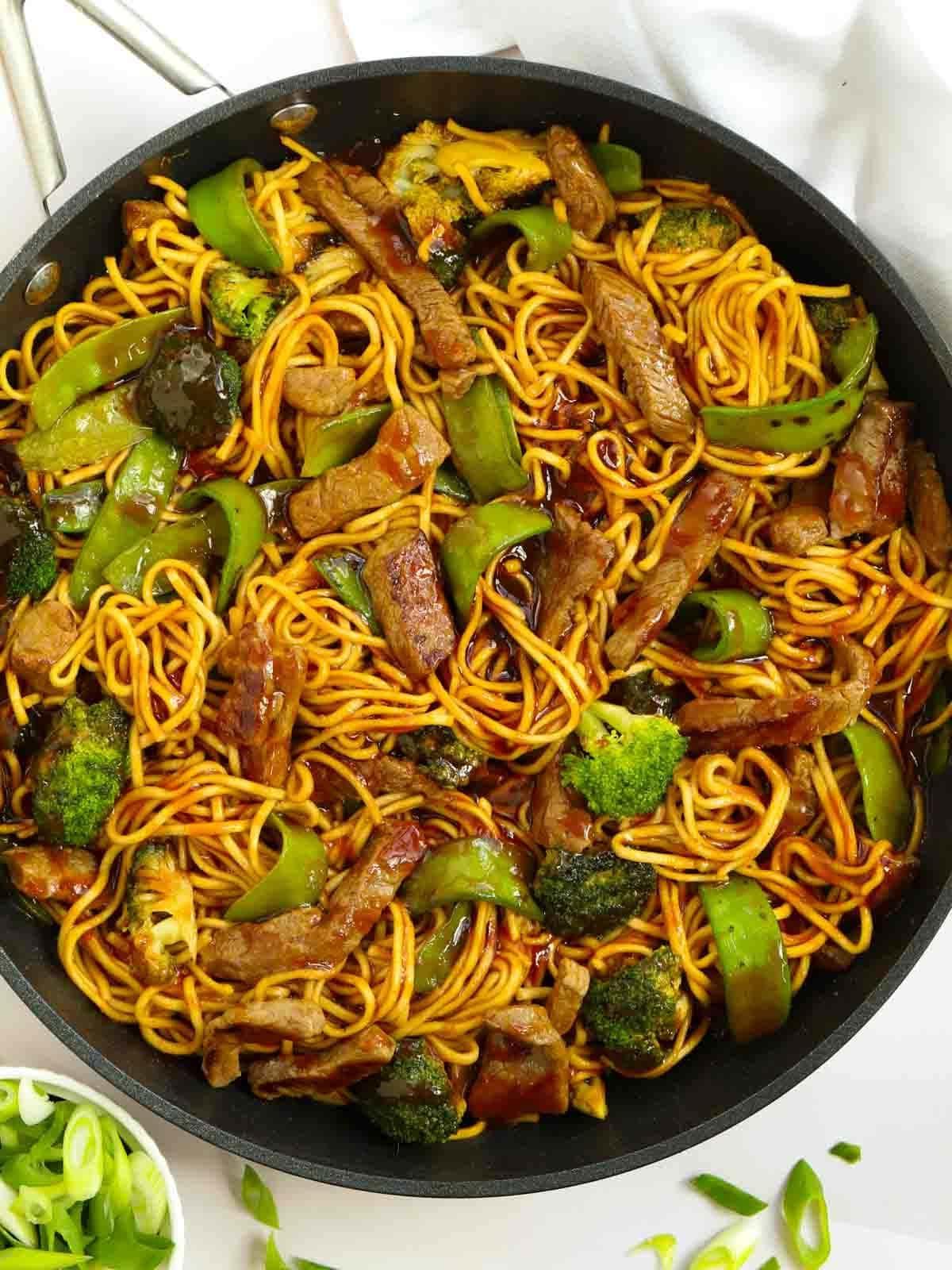 Manzo Glassato e Noodles {Monopadella} 2 Una grande padella piena di manzo appiccicoso e noodles, con verdure verdi e una salsa scura.