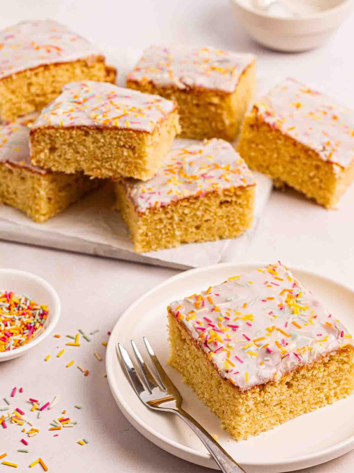 Torta Scolastica {Ricetta Facile!} 2 Un quadrato di Torta della Scuola su un piatto con una forchettina da dolce, con altri pezzi di torta sullo sfondo.