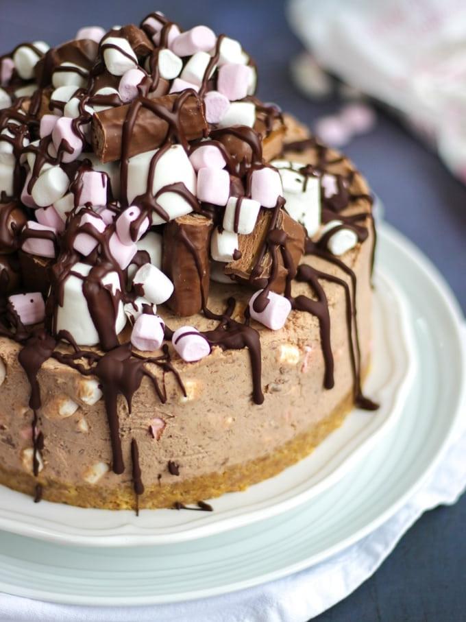 Cheesecake Rocky Road Senza Cottura 2 Cheesecake al cioccolato decorata con marshmallow e scaglie di cioccolato fondente, servita su piatti bianchi su sfondo grigio - Cheesecake Rocky Road.