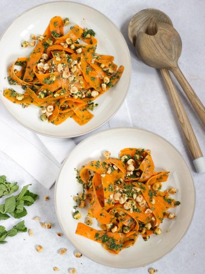 Due ciotole di insalata di carote con posate di legno per insalata e un tovagliolo bianco.
