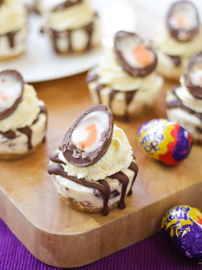 Mini Cheesecake Senza Cottura alle Uova Crema di Pasqua con un uovo crema tagliato sopra, su un tagliere di legno.