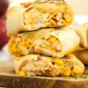 Facili Wrap di Pollo 11 Una pila di wraps di pollo cotti e affettati con formaggio e mais, pronti per essere serviti.