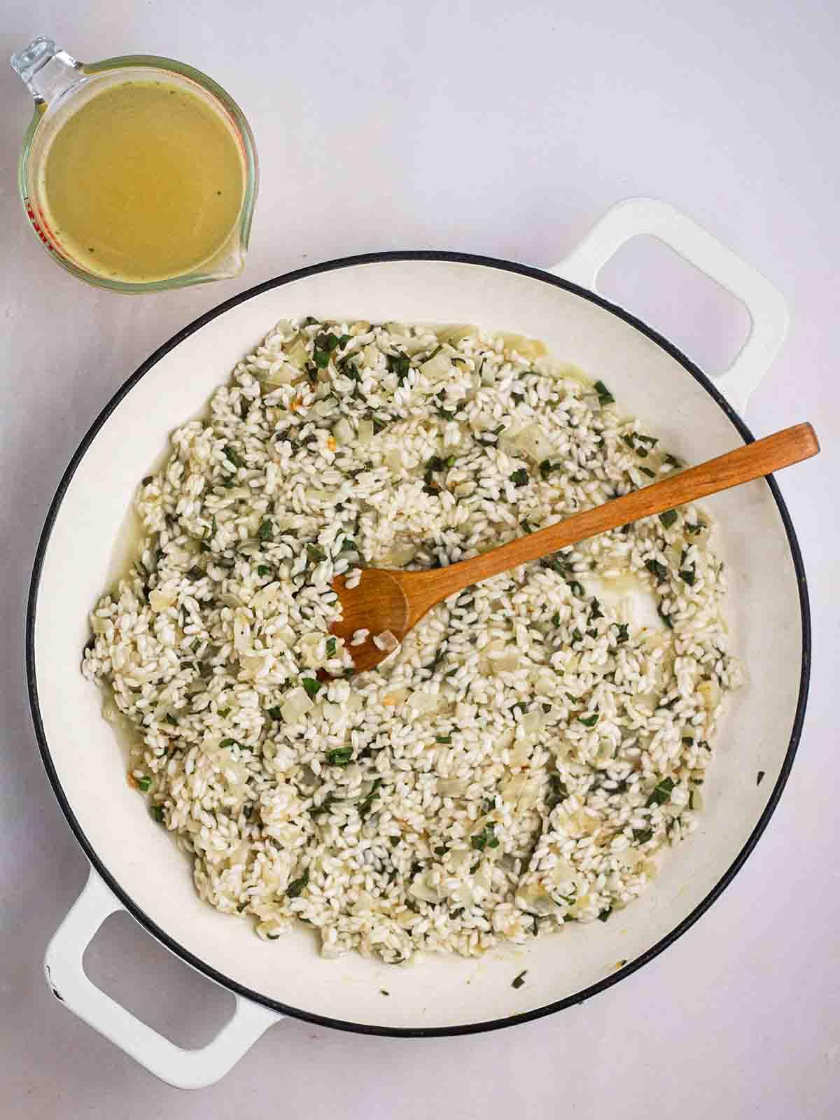 **Risotto di Zucca {Al Forno o Tradizionale}** 12 Un risotto in padella in cottura, con una brocca di brodo a lato.