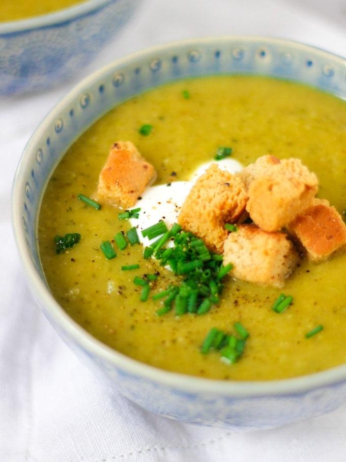 Zuppa Facile di Zucchine al Parmigiano 3 Una ciotola blu di vellutata di zucchine con panna acida, crostini e erba cipollina su sfondo bianco, vista laterale.