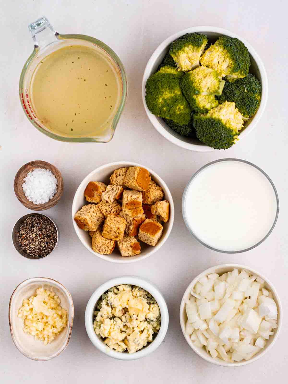 Zuppa di Broccoli e Stilton 3 Gli ingredienti per preparare la Zuppa di Broccoli e Stilton disposti in ciotole su un piano di lavoro bianco.