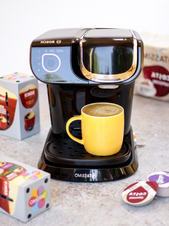 Macchina da caffè Tassimo con tazza gialla piena di caffè e capsule di caffè sullo sfondo per preparare la ricetta del caffè freddo con caramello salato.