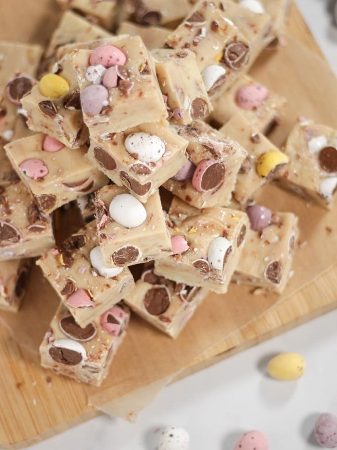 Pila di cubetti di fudge alle mini uova su un tagliere di legno.