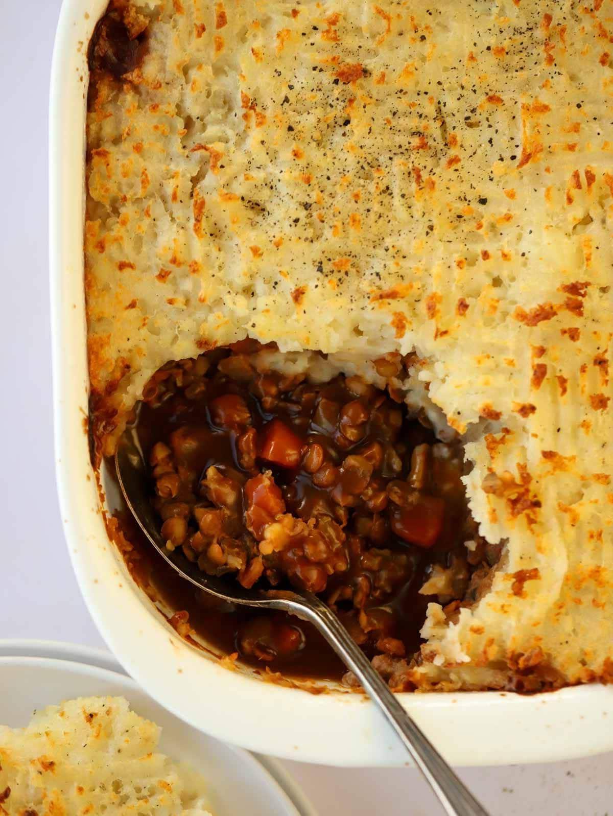 Il Pasticcio Vegetariano Definitivo 3 Un pasticcio vegetariano di lenticchie e patate, caldo e confortante, in una teglia con un cucchiaio, pronto per essere servito.