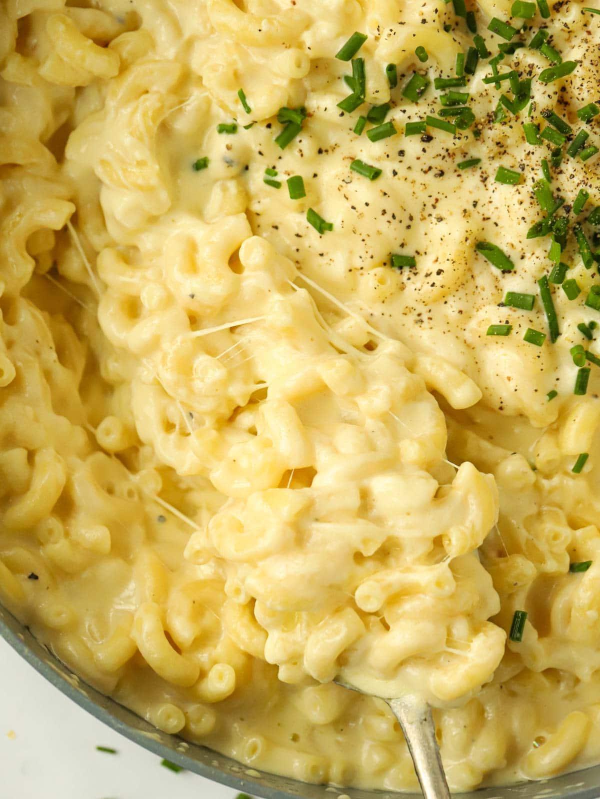 Primo piano di una pentola di Maccheroni al Formaggio semplici con il filo di formaggio che si allunga.