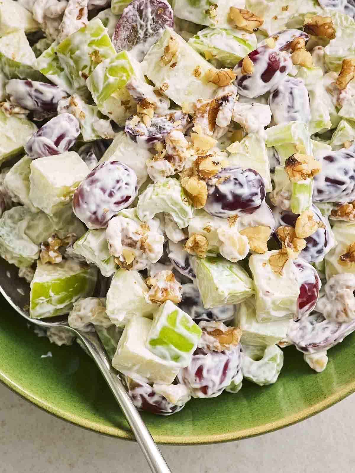 Una ciotola verde piena di Insalata Waldorf tritata, con un cucchiaio pronto per servire.