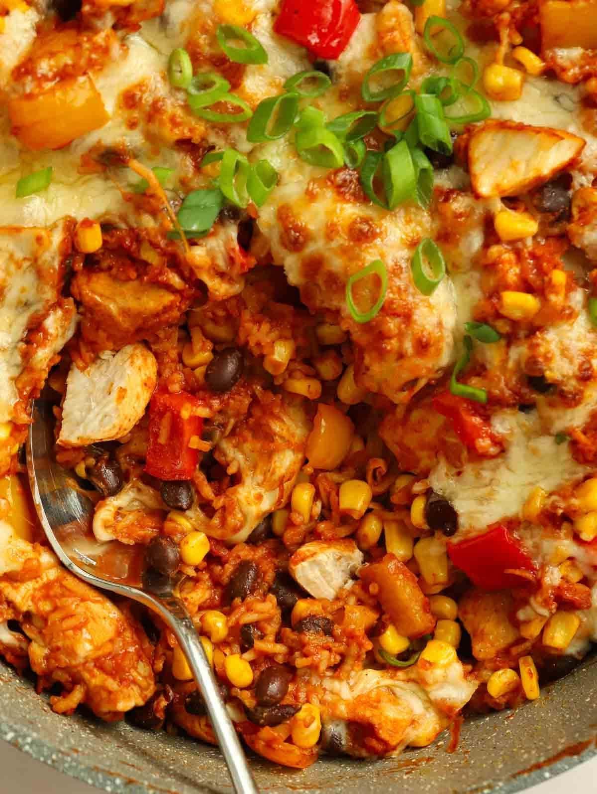 Un cucchiaio pronto a servire Pollo e Riso Messicano One Pot da una grande padella.