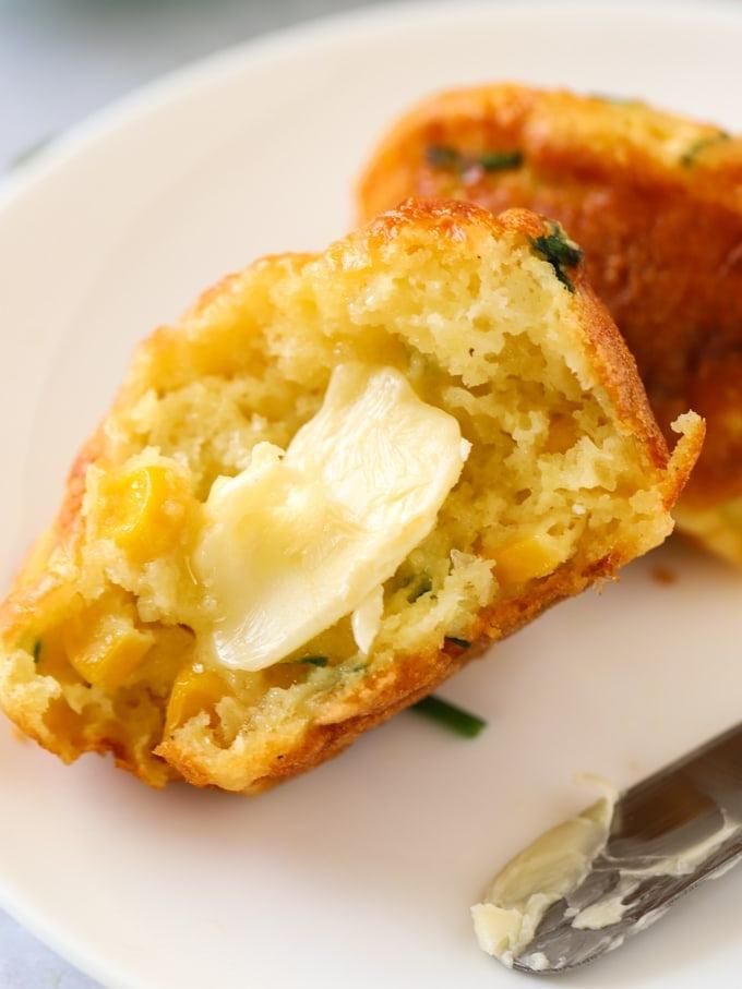 Muffin Salati {Formaggio e Mais} 3 Un muffin salato al formaggio su un piatto, tagliato a metà, con burro che si scioglie.