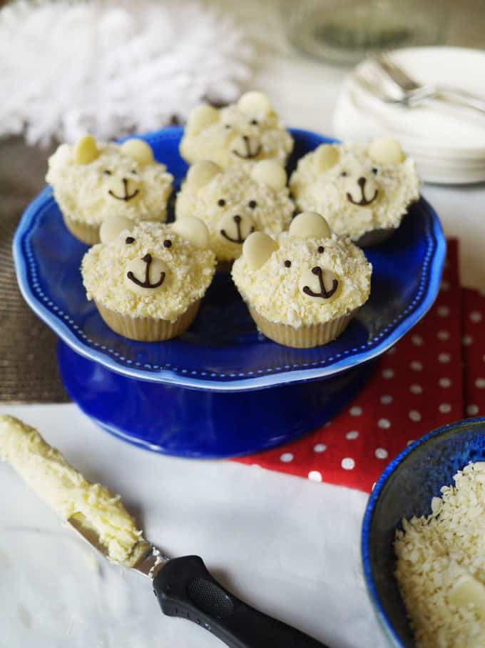Cupcakes Orso Polare {Ricetta Facilissima!} 3 Cupcake Orso Polare su un'alzata blu, con un tavolo festivo sullo sfondo.