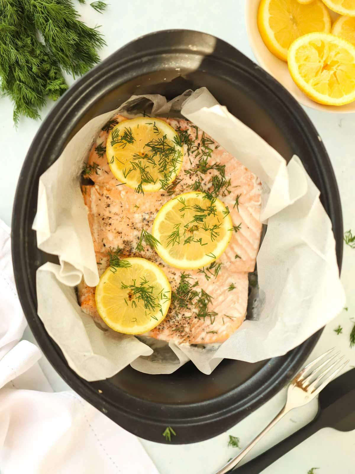 Semplice Salmone in Slow Cooker 3 Una slow cooker su una tovaglia bianca con salmone cotto all'interno, con limone sopra.