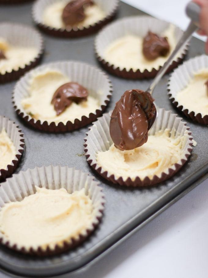 Foto di pirottini marroni in una teglia da muffin di metallo con l'impasto pronto per essere infornato.