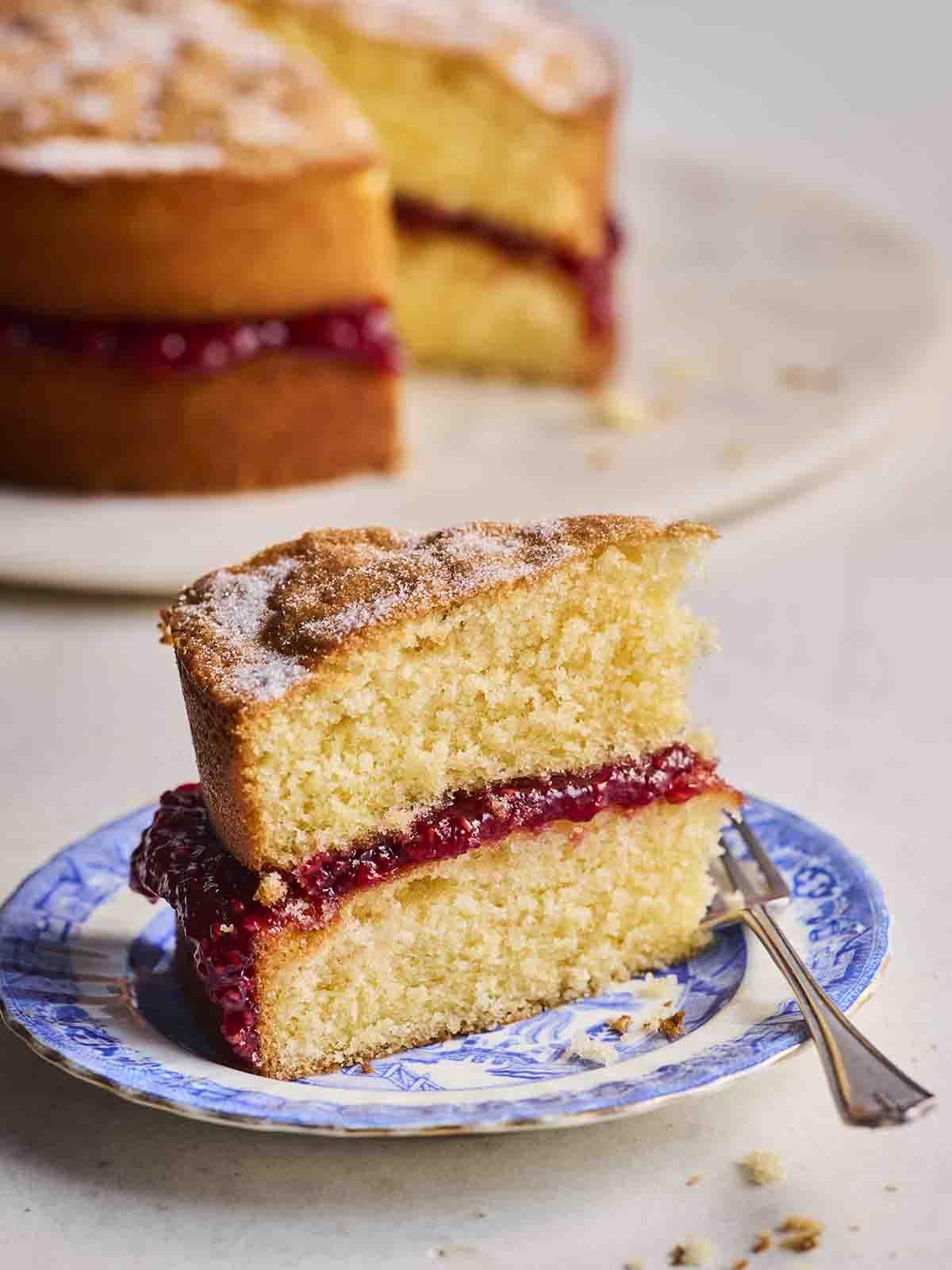 Torta Victoria Classica 3 Una fetta di Victoria Sponge su un piatto blu per torte con una forchetta, pronta per essere mangiata.