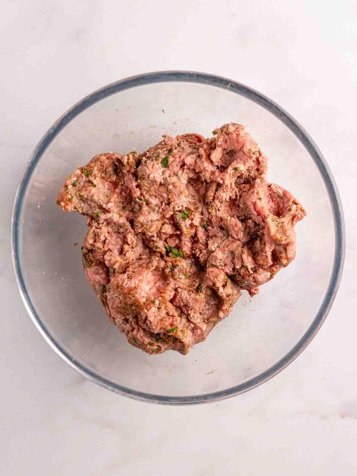 Facili Kofta di Agnello {con Tzatziki} 4 Carne macinata di agnello cruda mescolata con erbe in una ciotola di vetro, pronta per essere trasformata in kebab.