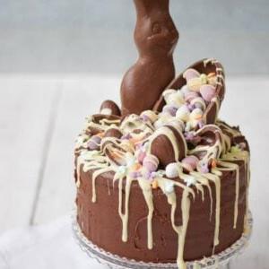 Torta al Cioccolato di Pasqua 4 Una torta al cioccolato di Pasqua molto cioccolatosa con molte uova di cioccolato e decorazioni a forma di coniglio e cioccolato bianco fuso, su un'alzata per torte.