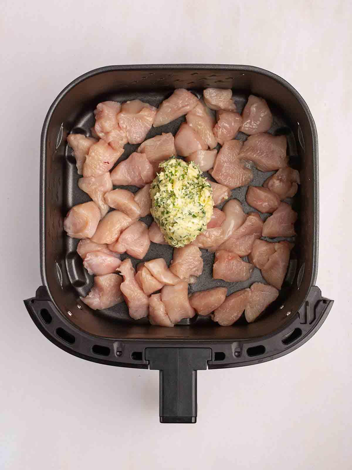 Pollo al Burro all'Aglio in Teglia con la Friggitrice ad Aria 4 Pezzi di pollo crudo in una friggitrice ad aria con una noce di burro all'aglio fatto in casa sopra per il passaggio 1 della ricetta del Pollo al Burro all'Aglio con Friggitrice ad Aria.