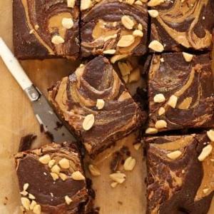Quadrati di brownies al burro d'arachidi tagliati su un tagliere con un coltello.