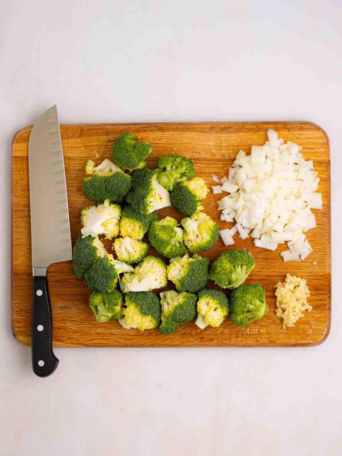 Zuppa di Broccoli e Stilton 4 Un tagliere con un coltello, broccoli e cipolla tritati pronti per preparare la Zuppa di Broccoli e Stilton.