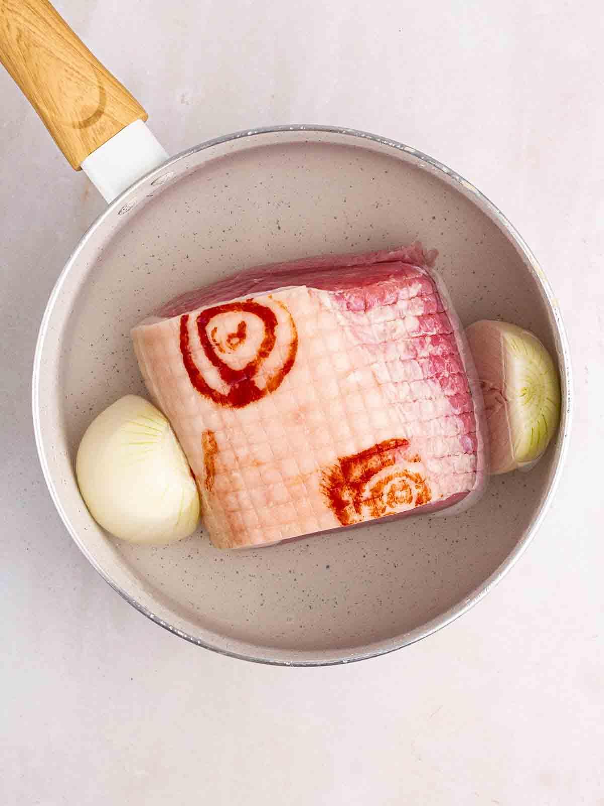 Un pezzo di gammon crudo in una pentola con cipolla per il passo 1 della ricetta Zuppa di Piselli e Prosciutto, fatta sul fornello.
