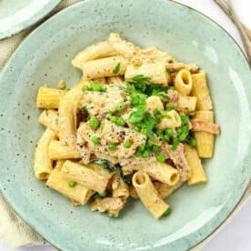 Pasta semplice e veloce con crema di formaggio su un piatto con piselli e prezzemolo sopra. Pronta da servire.