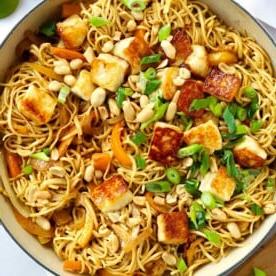 Noodles al burro di arachidi stile satay con halloumi in una grande padella.