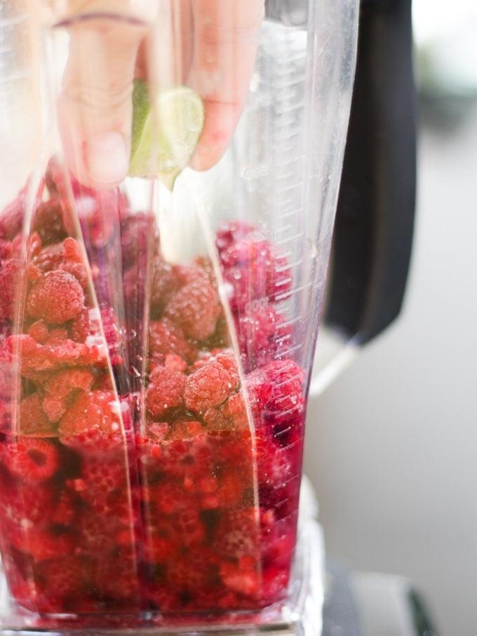 Lamponi congelati in un frullatore con lime che viene spremuto per la ricetta del Cocktail Ghiacciato al Gin e Lamponi.