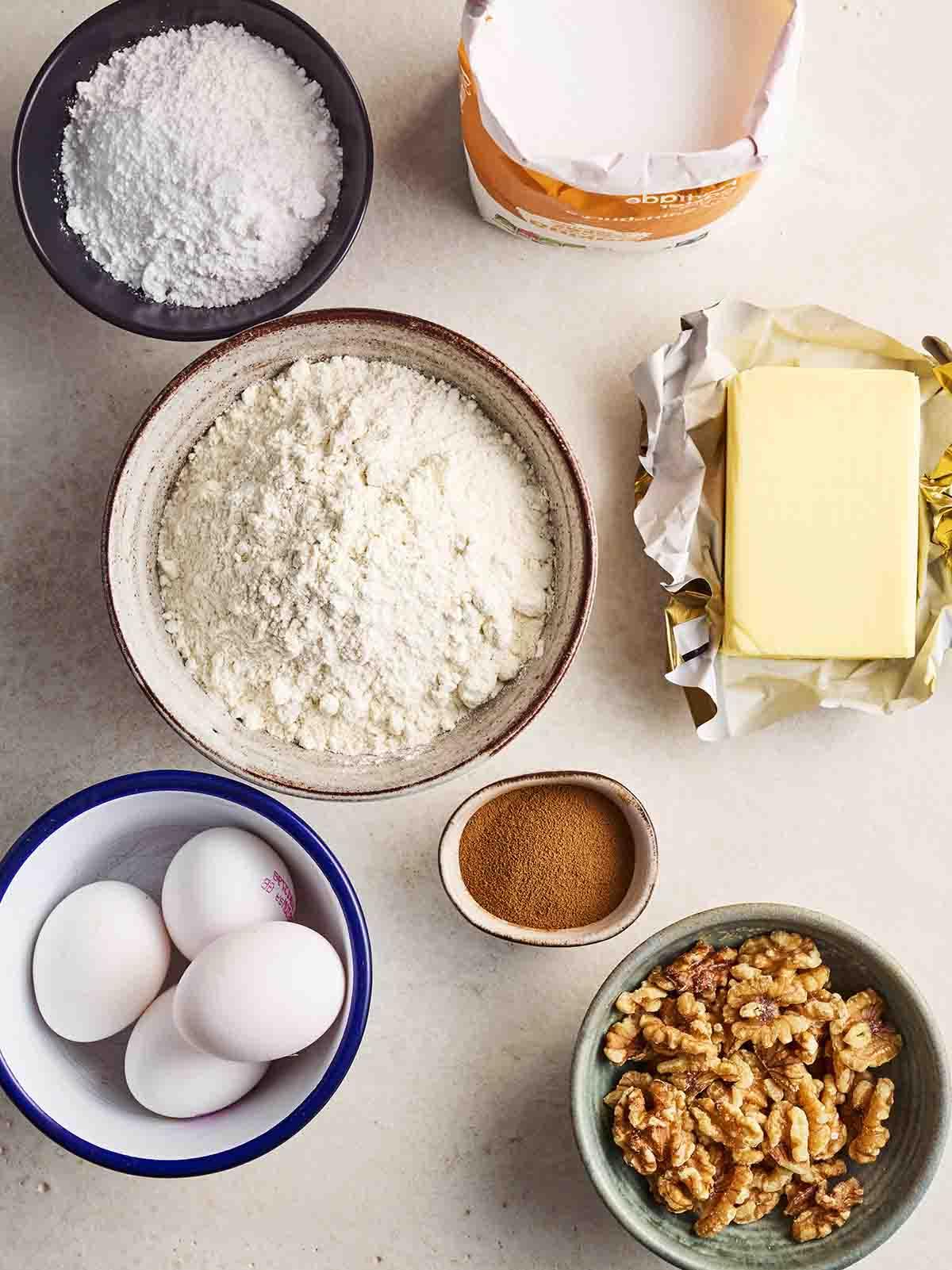 Gli ingredienti freschi e secchi necessari per la preparazione della Torta al Caffè e Noci, disposti ordinatamente su una superficie bianca.