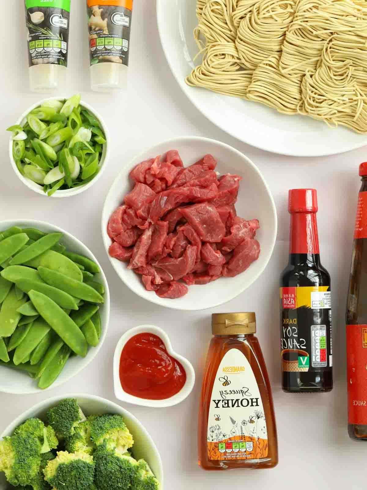 Manzo Glassato e Noodles {Monopadella} 4 Gli ingredienti per la ricetta Manzo Appiccicoso e Noodles disposti su un piano di lavoro, inclusi bistecca, verdure verdi, salse e noodles essiccati.