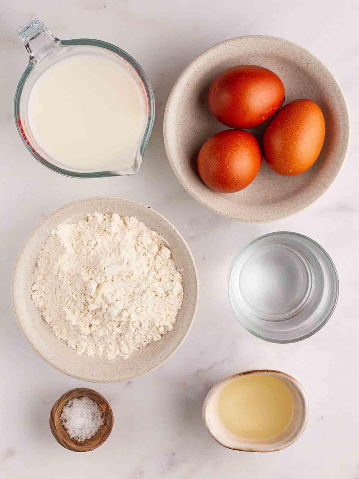 Yorkshire Puddings {Ricetta infallibile!} 4 Gli ingredienti per i Pudding dello Yorkshire disposti su un piano di lavoro. Tre uova, latte, farina 00, sale, olio e acqua.