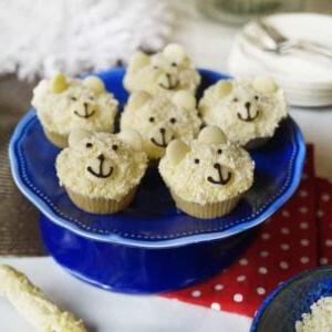 Cupcakes Orso Polare {Ricetta Facilissima!} 4 Cupcake al cioccolato bianco con il viso decorato come un orso polare, su un'alzata blu.