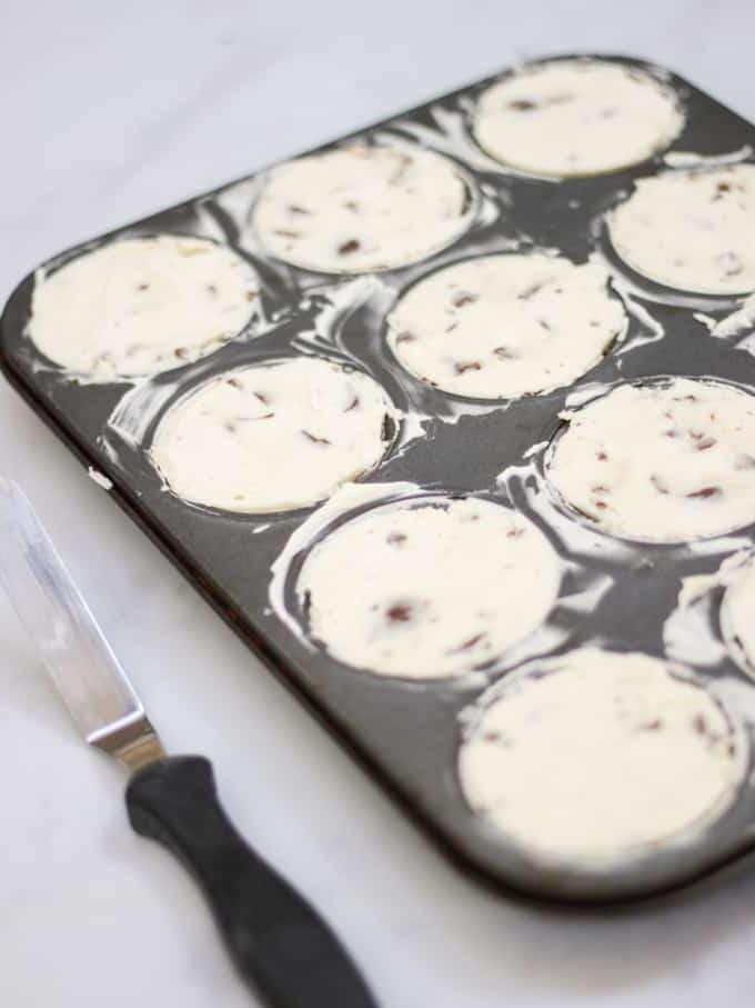 Mini cheesecake in uno stampo per muffin con spatola angolata su sfondo di marmo.