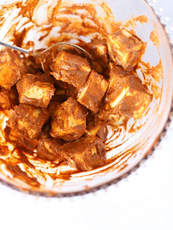 Facile Paneer Tikka {Per Griglia, Forno o Barbecue} 4 Cubetti di formaggio indiano paneer ricoperti di spezie e yogurt in una ciotola per il passaggio 1 della ricetta Paneer Tikka.