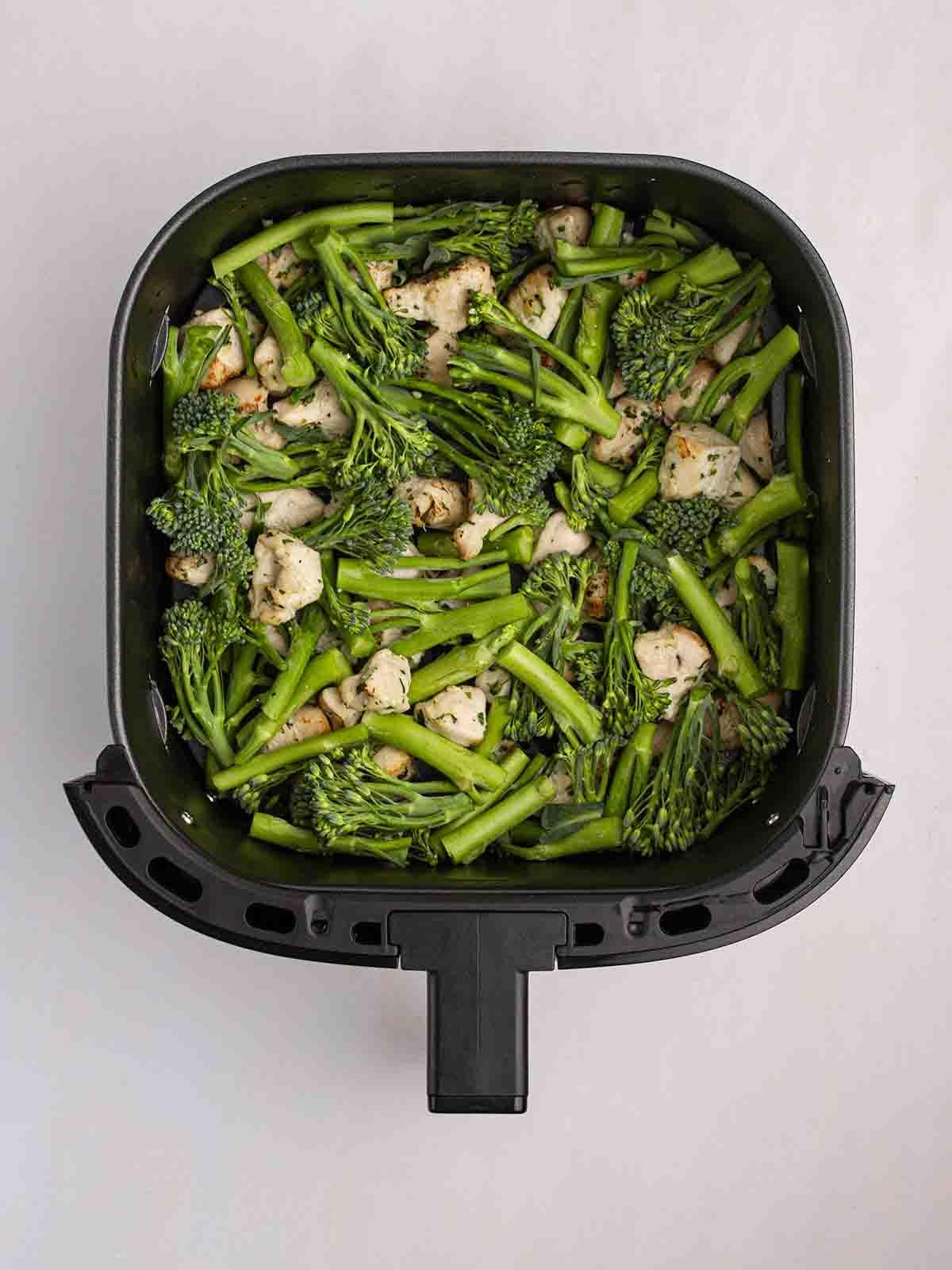 Pollo al Burro all'Aglio in Teglia con la Friggitrice ad Aria 5 Una friggitrice ad aria piena di pollo cotto e broccoli crudi per mostrare il passaggio 2 della ricetta del Pollo al Burro all'Aglio con Friggitrice ad Aria.