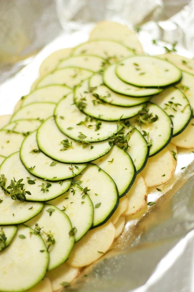 Fette di patate crude e zucchine disposte su alluminio.