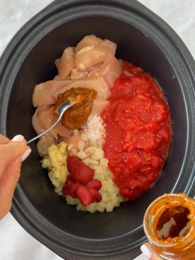 Passo 1 della ricetta per pollo tikka masala in slow cooker, con gli ingredienti crudi di pollo, pomodori, cipolla, concentrato di pomodoro, sale, aglio e pasta tikka nella pentola.