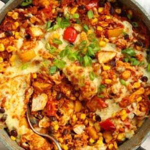 Una padella rotonda piena di pollo, riso, peperoni, fagioli e ricoperta di formaggio fuso per una ricetta di pollo messicano.
