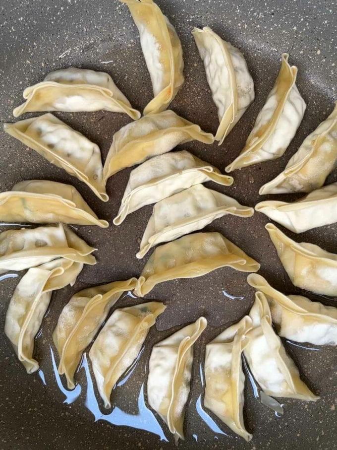 Ravioli gyoza in una padella per il passaggio 1 della ricetta della Zuppa di Gyoza.