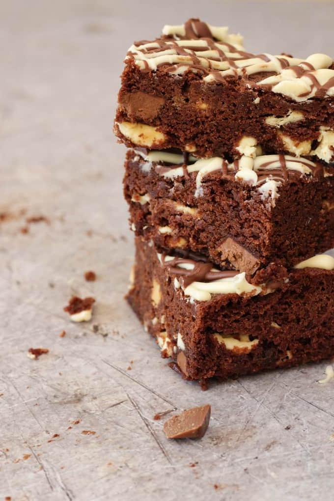 Una pila di tre brownies al cioccolato al microonde, ricoperti da una pioggia di cioccolato bianco fuso e ricchi di scaglie di cioccolato all'interno, su uno sfondo di metallo grigio.