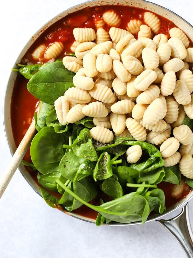 Gnocchi Facili al Forno 5 Spinaci e gnocchi aggiunti in una padella di salsa di pomodoro.