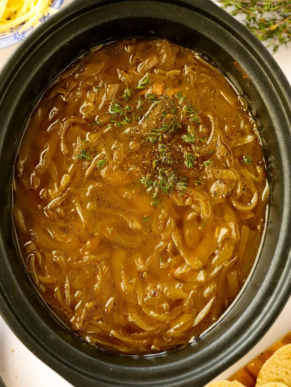 zuppa di cipolle francese guarnita con timo in una slow cooker nera