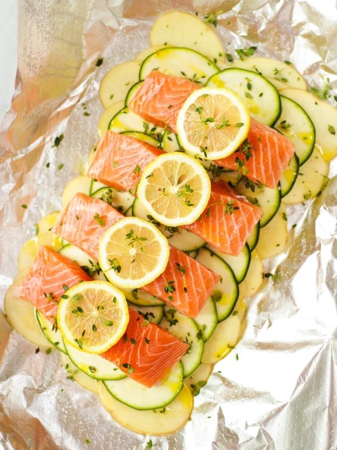 Filetti di salmone con fette di limone pronti per essere cotti su patate e zucchine affettate.